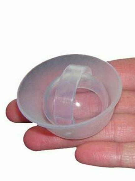 A hand holding a small round transparent plastic object. The object appears to be made of plastic and has a smooth shiny surface. It has a curved shape with a small opening at the top which is likely used to hold the object in place while it is being held in the palm of the hand. The background is plain white making the object stand out.