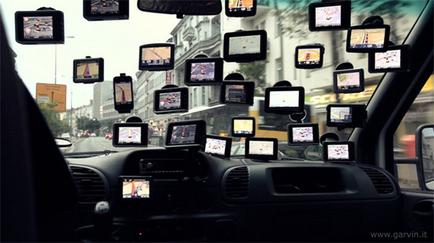 The interior of a car specifically the dashboard and the review mirror. The car is driving on a busy street with buildings and cars visible in the background. The dashboard is covered in multiple screens each displaying a different image or video. The screens are arranged in a grid-like pattern with some overlapping each other. The image appears to be taken from the driver's seat looking out the window at the street. The overall mood of the image is busy and bustling.