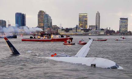 A view of a city skyline from the water. In the foreground there is a small boat with a red and white striped sail. The boat appears to be a rescue vessel as there are several other boats in the background. The sky is overcast and the water is choppy. In the center of the image there are two airplanes one white and one blue that are partially submerged in the water near the shore. The white airplane has a red stripe on the tail and the blue airplane has an orange stripe on its tail. The blue airplane is partially submerged with its wings spread out and its tail pointing towards the sky. There is also a large plume of smoke rising from the boat which could be from a fire or rescue operation. The city skyline is visible in the distance with tall buildings and skyscrapers.