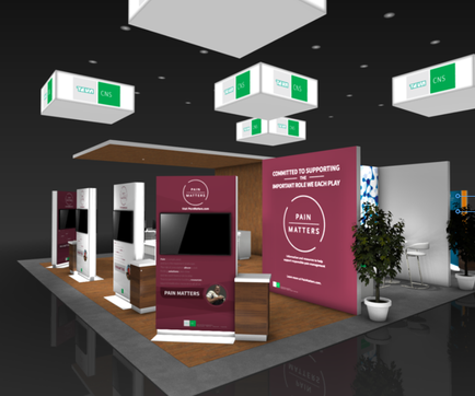 A trade show booth with a modern design. The booth has a black background with white and green accents. There are three white boxes hanging from the ceiling with green and white logos on them. On the left side of the booth there is a large pink banner with the words "Pain Matters" written in white text. Next to the banner there are two smaller white boxes with the same text. In front of the banners there appears to be a desk with a computer monitor and a plant in a white pot. The overall color scheme of the image is black white and green.