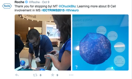 A screenshot of a tweet from Roche's Twitter account. The tweet reads "Thank you for stopping by MT @chuckle: Learning more about B Cell involvement in MS #ECTRIMS2015 #thneuro". On the left side of the image there is a photo of a man and a woman working together on a project. The man is wearing a blue shirt and glasses and is holding a tablet. He appears to be working on the project while the woman is looking at it intently. In the background there are other people and a large screen displaying information about the project. On the right side the photo shows a large blue sphere with white circles around it. The sphere appears to have a textured surface and is surrounded by a white background.