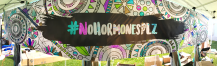 A large tent with a colorful and intricate design on it. The tent is set up on a grassy area with other tents and tables visible in the background. The design on the tent is made up of various geometric patterns and colors including circles squares triangles and rectangles. In the center of the tent there is a large black banner with the hashing "#NOMORRONESPLZ" written in white letters. The banner is slightly tilted to the right giving it a playful and whimsical feel.