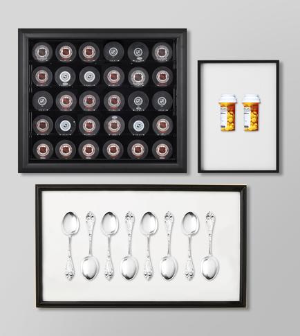Three framed pictures hanging on a white wall. The first picture on the top left is a black rectangular frame with a grid of small circular objects arranged in a grid-like pattern. The objects appear to be red and white in color. The second picture in the top right is a small white frame with two orange and yellow pills in it. The third picture is a set of six silver spoons arranged in two rows. The spoons have a classic design with a curved handle and a pointed tip. The frames are black and have a simple minimalist aesthetic.