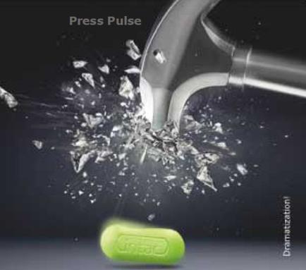 A green pill with the word "Press Pulse" written on it. The pill is being poured into a glass jar with a silver handle. The jar is filled with small pieces of glass that are splashing out of it creating a shower-like effect. The background is black making the green pill and the silver handle stand out. The image conveys a sense of urgency and danger.