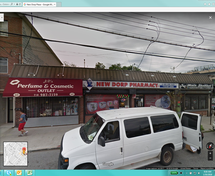A white van parked on the side of a street in front of a store named "Perfume & Cosmetic Outlet". The store has a red awning with the store's name written in white letters. The store is located on a corner of a brick building with a sign that reads "New Dorp Pharmacy". There are several other stores visible in the background including a perfume and cosmetic outlet and a new Dorp pharmacy. The sky is overcast and there are power lines running across the street.