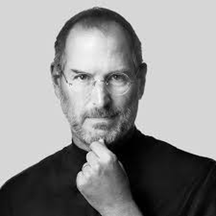 A black and white portrait of Steve Jobs the former CEO of Apple Inc. He is shown in a close-up shot with his chin resting on his hand. He has a serious expression on his face and is looking directly at the camera. His hair is neatly combed back and he has a beard and mustache. He appears to be in his late 40s or early 50s with a slight smile on his lips. The background is plain and minimalist making the focus of the image the focal point.