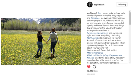 Two young women walking hand in hand through a field of yellow flowers. They are both wearing casual clothes and appear to be in a peaceful and serene environment. The field is surrounded by mountains and trees and the sky is blue and clear. The women are smiling and seem to be enjoying each others company. On the right side of the image there is a text that reads "Sophia Bush" and a profile picture of the woman on the left.