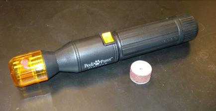 A black flashlight with an orange LED light on the side. The flashlight has a black handle and a black body with the brand name "Polaris" written on it in white letters. The LED light is turned on and appears to be turned on. Next to the flashlight there is a small white object possibly a screwdriver bit which is likely used to remove the flashlight from the surface. The background is a black surface.