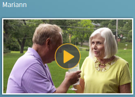 An elderly couple a man and a woman standing in a park or garden. The man is on the left side of the image wearing a purple polo shirt and is holding a glass of wine in his hand. He is facing the woman who is wearing a yellow top and has white hair. They are both smiling and appear to be engaged in a conversation. In the background there are trees and a grassy lawn. There is a yellow play button in the bottom right corner indicating that the image is a screenshot from a video.