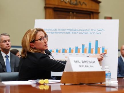 Heather Bresch (CEO of Mylan N.V.) interprets a bar chart with the title EpiPen Auto-Injector Wholesale Acquisition Cost (WAC) Average Revenue (Net Price) to Mylan Per 2-Pack. Men in business suits are visible in the background. She appears to be in a courtroom or similar facility.