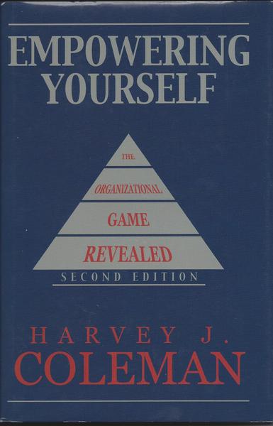 The cover of a book titled "Empowering Yourself: The Organizational Game Revealed" by Harvey J. Coleman. The cover is predominantly blue with white text. The title of the book is written in large bold font at the top followed by the author's name in smaller font. Below the title there is a pyramid-shaped graphic with the words "Organizational Game" and "Revealed" written on it. The pyramid is divided into three sections each with a different color - red white and blue. The second edition is written at the bottom of the pyramid. The book appears to be a hardcover with a glossy finish.