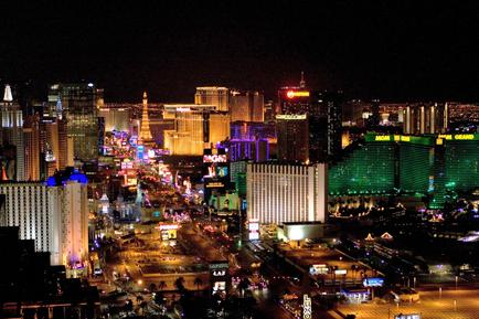 A panoramic view of the Las Vegas Strip at night. The city is lit up with colorful lights creating a vibrant and lively atmosphere. The buildings are tall and modern with a mix of different styles and shapes. The Las Vegas strip is visible in the background with the iconic Eiffel Tower in the center. The sky is dark making the colors of the lights stand out even more. The image is taken from a high vantage point looking down on the city below.