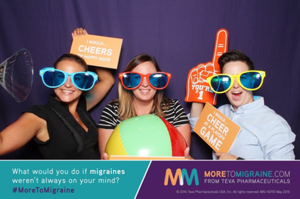 Three young women posing for a photo in a photo booth. They are all wearing colorful sunglasses and holding up signs that say "Cheers" and "Cheer Game". The woman on the left is wearing a black top and the woman in the middle is holding a beach ball. The background is a purple curtain. The text on the image reads "What would you do if migraines weren't always on your mind? #MoreToMigraine".
