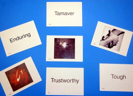 A collection of six cards arranged in a grid-like pattern on a blue background. Each card has a different word written on it - "tamper" "Enduring" "Trustworthy" "Tough" and "A1". The first card on the top left has the word "enduring" written in black text. The second card in the middle has a black and white photograph of two hands holding each other. The third card has an image of a brick wall with a cross in the center. The fourth card has the words "Trustworthiness" written below it in white text. All the cards appear to be blank with no text or images on them.