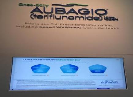 A digital screen with the logo of adagio (adagio Terifluomide) and the text "Please see Full Prescribing Information including boxed WARNING within the booth." Below the logo there is a message that reads "Don't let me therapy define their day". The screen is divided into three sections each with a different color - blue green and yellow. The blue section has a pie chart the green section has three blue sections and the yellow section has two blue sections. The text is written in black font and is centered on the screen. The background of the screen is a light beige color.
