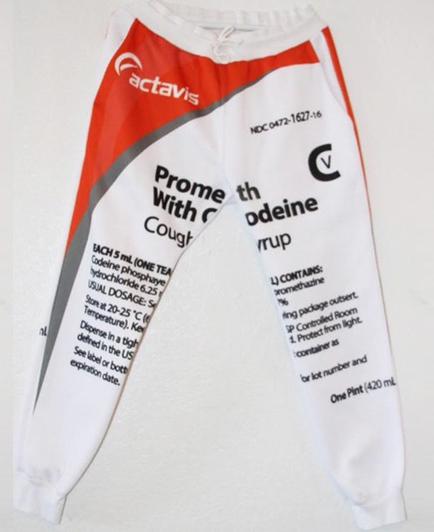 A pair of white sweatpants with a red and black design on the left leg. The design features the brand name "activist" in bold red letters at the top followed by the text "Promethodeine with Cough" in black letters. Below the text there is a list of ingredients and their corresponding numbers. The ingredients are arranged in a grid-like pattern with each ingredient listed in a separate column. The pants appear to be made of a soft comfortable material and have a drawstring waistband. The background of the image is plain white.