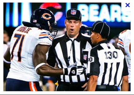 A football game between the Chicago Bears and the New England Patriots. The Bears player number 71 is being congratulated by a referee number 130 who is wearing a black and white striped jersey. The referee is standing in front of the Bears player and appears to be speaking to him. The background shows the field and the stands of the stadium. The image appears to have been taken during a game.
