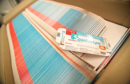 A cardboard box with a blue and red striped fabric inside. The fabric appears to be made of a soft textured fabric with vertical stripes in shades of blue red and white. On top of the fabric there is a white label with the brand name "season-lyon" written in blue and orange. The label also has a arcade and the number "80" printed on it. The box is sitting on a beige surface.