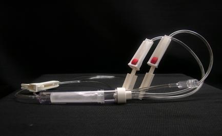 A medical device with a long thin tube attached to it. The tube is made of clear plastic and has a white cap on one end. On the other end there are two white plastic tubes with red caps. The tubes are connected to a white cable that runs along the length of the tube. The background is black making the device stand out. The device appears to be a syringe or a device used for medical purposes.