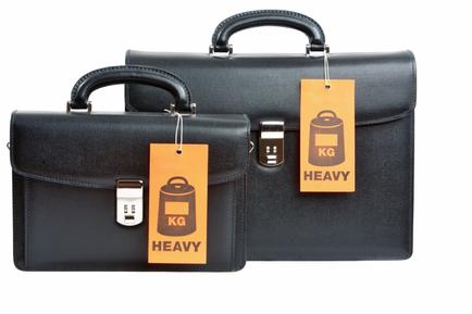 Two black briefcases with orange tags attached to them. The bags are made of leather and have a handle on top for easy carrying. The tags have the words "KG" and "HEAVY" written on them in white text. There is also an image of a kettle on one of the tags. The background is white making the black bags stand out.