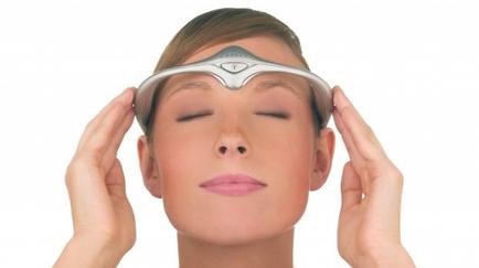 A young woman with her eyes closed resting her head on her hands. She is wearing a silver-colored headband with a triangular design on it. The headband appears to be made of metal and has a curved shape. The woman's face is not visible in the image but her hair is pulled back in a neat bun. She has a neutral expression on her face and is looking off to the side. The background is plain white.