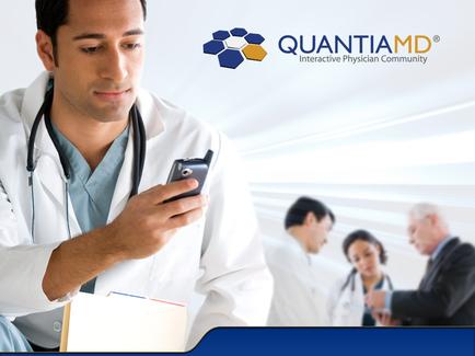 A young man wearing a white lab coat and a stethoscope around his neck. He is holding a mobile phone in his hand and appears to be looking at it intently. In the background there are three doctors and a patient. The image also has the logo of quantum an interactive physician community on the top right corner. The background is blurred but it seems to be a medical office or clinic setting.