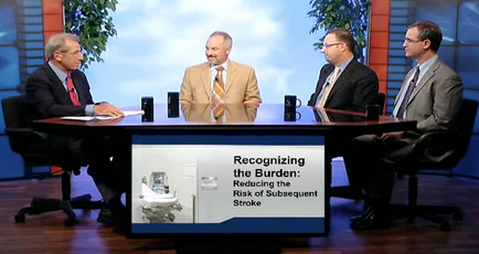 Four men sitting around a conference table in a news studio. They are all wearing suits and appear to be engaged in a conversation. The man in the center is holding a microphone and appears to be speaking while the other three men are listening attentively. On the table there are two coffee mugs and a piece of paper. In the background there is a large screen with a headline that reads "Recognizing the Burden: Reducing the Risk of Subsequent Stroke".