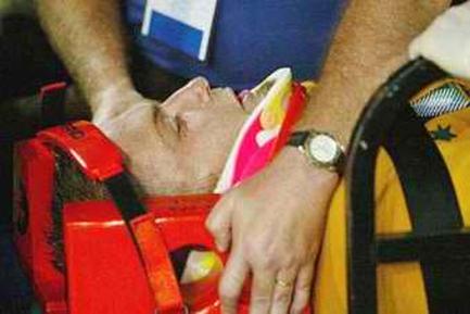 A person's hand holding a red lifebuoy. The person is wearing a blue t-shirt and a watch on their wrist. The background is blurred but it appears to be an indoor setting with a yellow chair visible on the right side of the image. The focus is on the hand and the person's arm. It seems like the person is receiving medical attention or treatment.