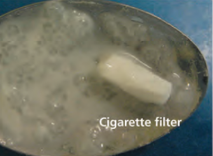 A close-up of a cigarette filter in a bowl. The filter is white and appears to be made of plastic or a similar material. It is in the center of the image and is slightly tilted to the right. The background is a light blue color. The text on the image reads "Cigarette filter".