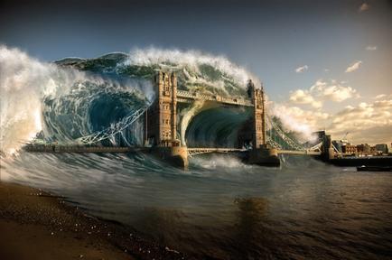 A photograph of the Tower Bridge in London UK. The bridge is a suspension bridge that spans across the River Thames. The image is taken from a low angle looking up at the bridge and the waves crashing against it. The waves are large and powerful creating a dramatic scene. The sky is blue with a few clouds and the sun is setting in the background casting a warm glow over the scene. On the right side of the image there is a city skyline visible with buildings and skyscrapers. The water is calm and still reflecting the colors of the sky.