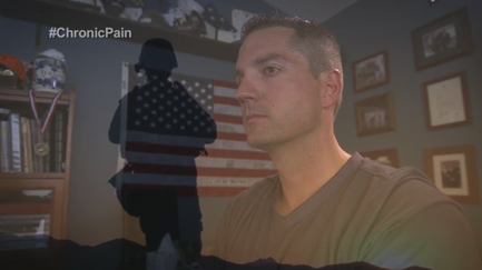 A screenshot from a video call. It shows a man in a living room with an American flag in the background. The man is wearing a green t-shirt and is looking off to the side with a serious expression on his face. On the left side of the image there is a silhouette of a person wearing a military uniform and a helmet. The text on the image reads "#ChronicPain".