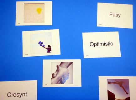 A collage of six square photographs arranged in a grid-like pattern on a blue background. The photographs are arranged in two rows and three columns. The first photograph on the top left is a square with a yellow sun in the center. The second photograph is a black and white photograph of a person holding a bunch of blue balloons. The third photograph is an abstract photograph of two hands holding each other. The fourth photograph is of a hand reaching out towards the sky. The fifth photograph is titled "Easy" and the sixth photograph is labeled "Optimistic". At the bottom left corner of the image there is a label that reads "present".