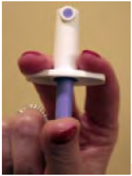 A hand holding a small white and blue object. The object appears to be made of plastic and has a cylindrical shape with a flat base. The top of the object has a small blue button on it which is likely used to control the flow of liquid or gas. The hand is holding the object with one hand and the other hand is gently cradling it. The background is a plain beige color.