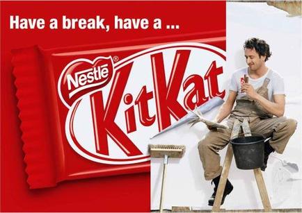 A man sitting on a ladder and painting a wall with a KitKat chocolate bar. He is wearing a white t-shirt khaki pants and black shoes. He has a paintbrush in his hand and is holding a paint roller in his other hand. The background is white and there is a red Nestle KitKat logo on the left side of the image. The text on the image reads "Have a break have a..."