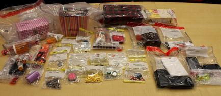 A collection of various items scattered on a wooden table. There are several items in plastic bags including a pink and white striped box a red and black plaid box and a black and white checkered box. The items are arranged in a scattered manner with some overlapping each other. Some of the items appear to be small items while others are larger and more compact. There is also a small black purse with a red ribbon tied around it. The table appears to be in a room with a white wall in the background.