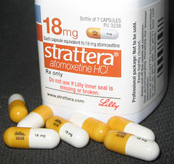 A white container of Strattera Atomoxetine HCI 18mg tablets. The container is cylindrical in shape and has a label on it that reads "18mg" in bold orange letters. Below the label there is a description of the product which states that the tablets are available for purchase at 7 capsules. <br /><br />There are several white and yellow pills scattered around the container. The pills are of different sizes and shapes with some being white and others being yellow. The label also says "Do not use if the inner seal is missing or broken."<br /><br />The container is placed on a black surface and there are a few more pills scattered next to it. The background is blurred so the focus is on the container and the pills.