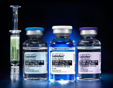 Three prefilled syringes of Gablofen. All three syringes have blue caps and white labels with the brand name and dosage information printed on them. The background is black making the syringes stand out. The image appears to have been taken in a laboratory setting.