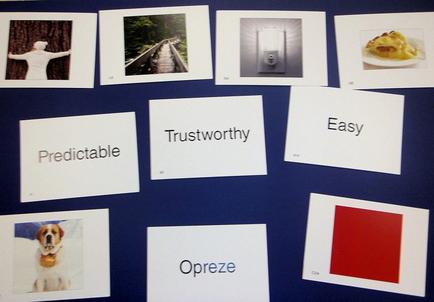 A collection of nine white cards arranged in a grid-like pattern on a blue background. Each card has a different word written on it in black text. The word "Predictable" is written in bold letters at the top left corner of each card. Below that there is a photograph of a person standing on a wooden bridge with their arms stretched out in front of them. The first card on the top right corner has a picture of a plate of food with a fork and knife on it. The second card in the center has the word "Trustworthy" written in a cursive font. The third card has an image of a dog with a red square in the bottom right corner. The fourth card has the words "Easy" and "Opreze" written on the bottom left corner. Overall the image appears to be a visual representation of the concept of predicting trustworthy and easy.