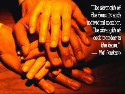 A group of hands stacked on top of each other forming a circle. The hands appear to be of different sizes and colors with the fingers slightly curled and the palms facing upwards. The background is blurred but it appears to be a wooden table or desk. On the right side of the image there is a quote from Phil Jackson that reads "The strength of the team is each individual member. The strength of each member is the team." The quote is written in white text on a black background.
