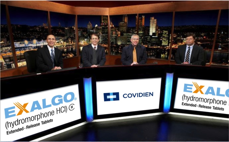 Four men sitting at a desk in front of a large window with a view of a city skyline at night. They are all wearing suits and appear to be in a news studio. On the desk there are three large screens displaying the logos of Exalgo (Hydromorphone HCI Extended-Release Tablets) and Covidien. The men are smiling and looking at the camera. The background shows a cityscape with tall buildings and skyscrapers.