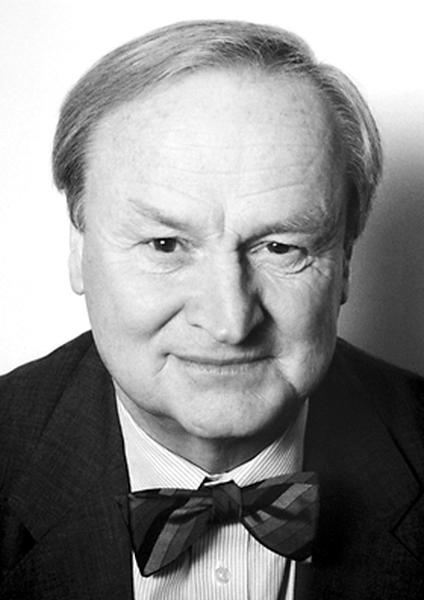 A black and white portrait of an older man. He is wearing a suit and a bow tie and his hair is neatly combed back. He has a serious expression on his face and is looking directly at the camera. The background is blurred so the focus is on the man's face. He appears to be in his late 60s or early 70s.