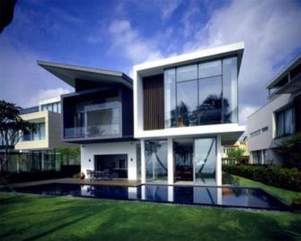 A modern two-story house with a large swimming pool in the backyard. The house has a white exterior with large glass windows on the second floor and a black roof. The pool is surrounded by a well-manicured lawn and there are trees and bushes in the background. The sky is blue with a few clouds and the overall atmosphere of the image is peaceful and serene.