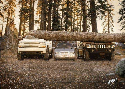 Three cars parked in a forest. The car on the left is a white Chevrolet silvered the car in the middle is a silver Chevrolet Tahoe and the one on the right is a black Hummer H2. All three cars are carrying a large tree trunk over their heads. The trees in the background are tall and have green leaves. The ground is covered in fallen leaves and there are rocks scattered around. The sky is blue and the overall mood of the image is peaceful and serene.