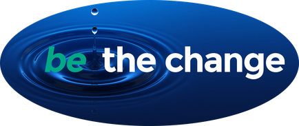 A graphic design with a blue background. In the center of the image there is a circular shape with a drop of water falling into it. The drop is in the shape of a circle and is slightly tilted to the right. The word "be the change" is written in white capital letters in a modern sans-serif font. The overall design is simple and minimalist.