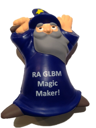 A close-up of a toy figure of a wizard. The figure is wearing a blue robe with the words "RA glum Magic Maker!" written on it in white letters. The wizard has a long grey beard and a pointed hat with a yellow star on top. He is holding a wand in his right hand and has a mischievous expression on his face. The background is white.