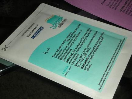 A white packet with a blue label on it. The label has the brand name "endoderm" written in bold black letters at the top. Below the label there is a description of the product which is written in black text. The packet appears to be sealed and is lying on a black surface. The background is blurred but it seems to be a desk or table with other items scattered around.