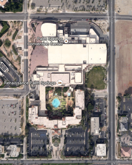 This is an aerial photograph of a city block in Palm Springs California with annotations intended for use as a map. It shows the location of the Renaissance Palm Springs Hotel (at the bottom) and how it is directly connected to the Palm Springs Convention Center (at the top). The location is bounded by North Calle Alvarado on the west East Amado Road on the north North Avenida Caballeros on the east and East Tahquitz Canyon Way on the south with parking lots and undeveloped land along the outer border of the image.