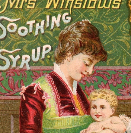 An advertisement for Mrs. Windsor's Soothing Syrup. It features a young woman holding a baby in her arms. The woman is wearing a red and green dress with a white collar and a red shawl draped over her shoulders. She has her hair styled in an updo and is looking down at the baby with a gentle expression on her face. The baby is a young girl with blonde hair and is smiling at the woman. The background is a greenish-blue color with a floral pattern. Above the woman there is a gold border with the words "Mrs. Windsor" written in a cursive font. The overall style of the advertisement is vintage and ornate.