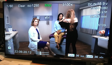 A screenshot of a medical video on a TV screen. It shows three women in a room with a desk and a computer monitor in the background. The woman on the left is wearing a white lab coat and is sitting on a chair while the woman in the middle is standing and appears to be explaining something to the other two women. The third woman is sitting in a chair with her back to the camera and the fourth woman is standing next to her. All three women are looking at the TV screen and appear to be engaged in a conversation. On the top left corner of the screen there is a text that reads "1/60 Clear ISO 1250 stay" and on the top right corner there are numbers that read "3100K" "DC IN 15.9V" "1920x1080" "29.97P" "SR-SQ 444" and "studs". On the bottom left corner the date "22:06:20:12" is displayed indicating that the video is being recorded on the TV.