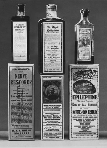 A group of six bottles of medicine arranged in a pyramid-like formation. All the bottles appear to be old and worn with some of the labels showing signs of wear and tear. <br /><br />The first bottle on the top left is labeled "Nerve Restorer" and has a label that reads "Dr. R. E. Ellington's Nerve Restorer". The second bottle is labeled "Epileptine" and is labeled as "King of All Remedies". The third bottle is titled "Nature's Own Remedy" and contains a label with an illustration of a man's face and the words "World Epilepticine". The fourth bottle has a description which states that it is "King-of-All Remedy". The fifth bottle has an image of a woman's face and the sixth bottle has the same label as the first bottle.<br /><br />The background is plain and the overall color scheme of the image is black and white.